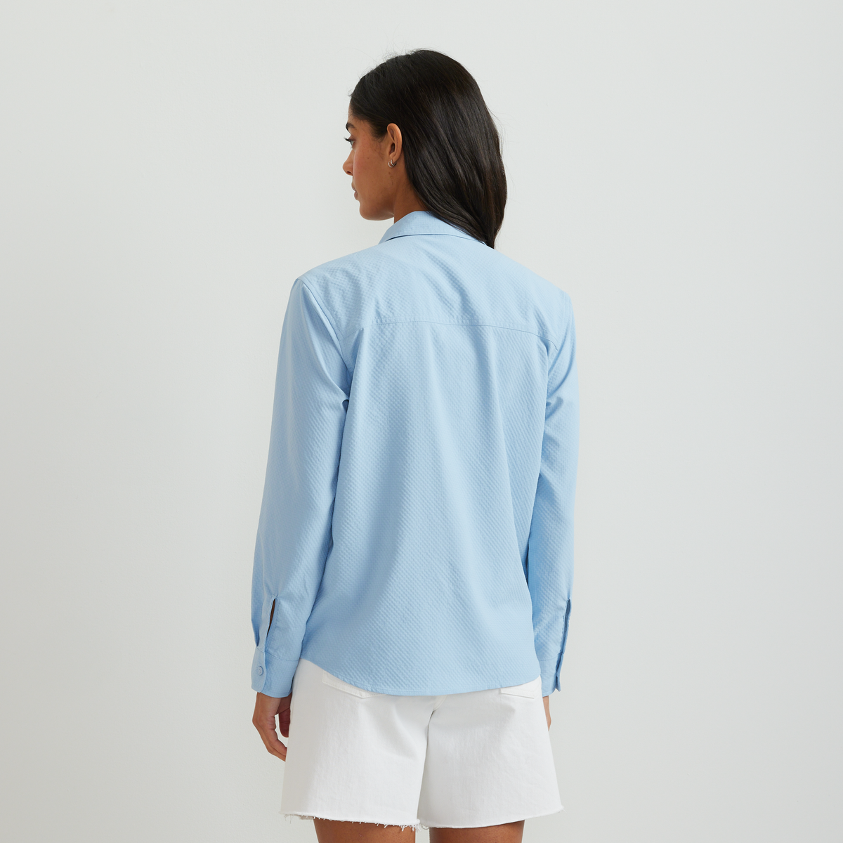 Light blue long-sleeve shirt with textured fabric and button front, shown on model wearing white shorts.