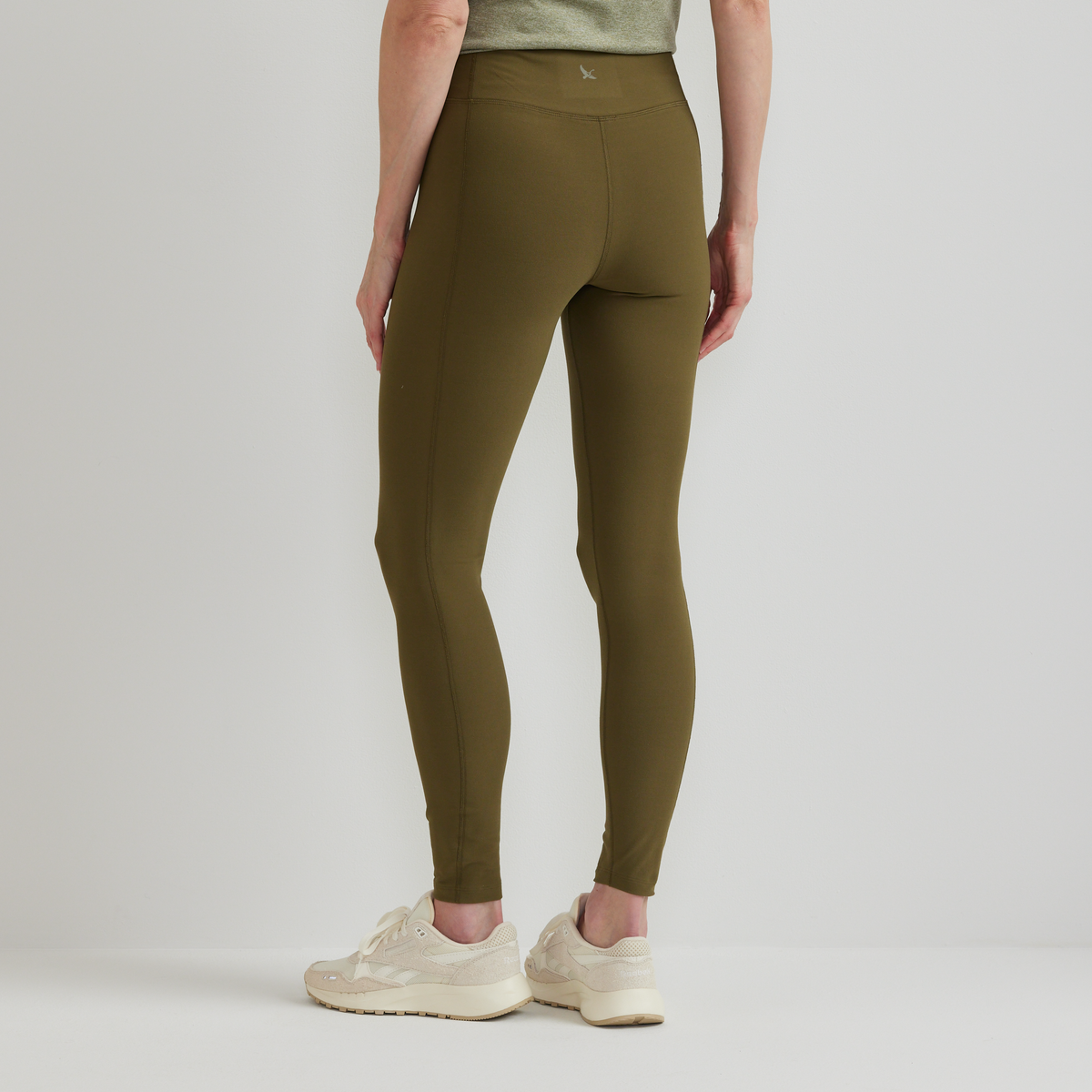 Olive green high-rise leggings with a center seam, worn with a gray top and cream sneakers.