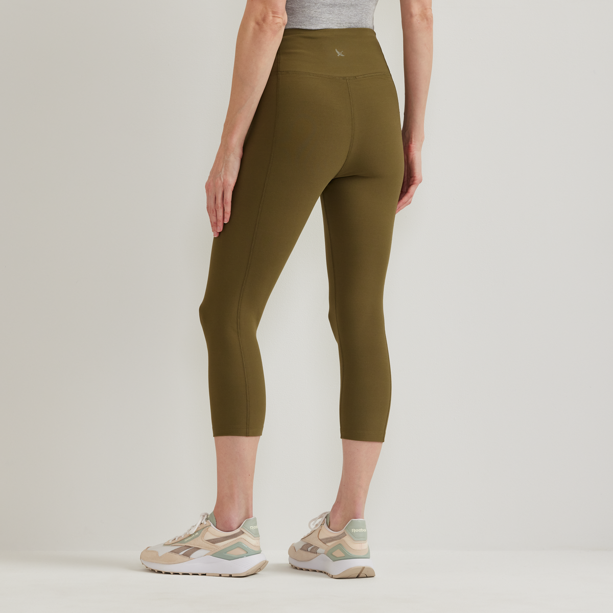 Olive green high-rise capri leggings with side seams, worn with gray top and tan athletic shoes.