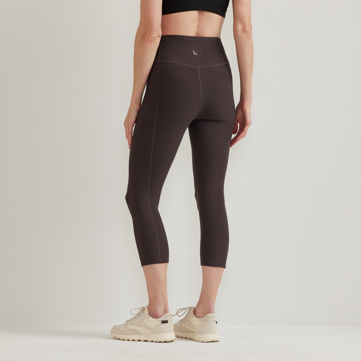 Black high-rise capri leggings with side seam detail, worn with cream sneakers.