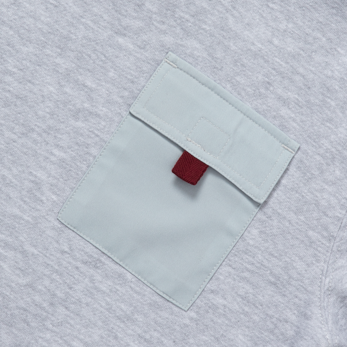 Gray fleece crewneck with white chest pocket and maroon fabric detail on gray textured background.