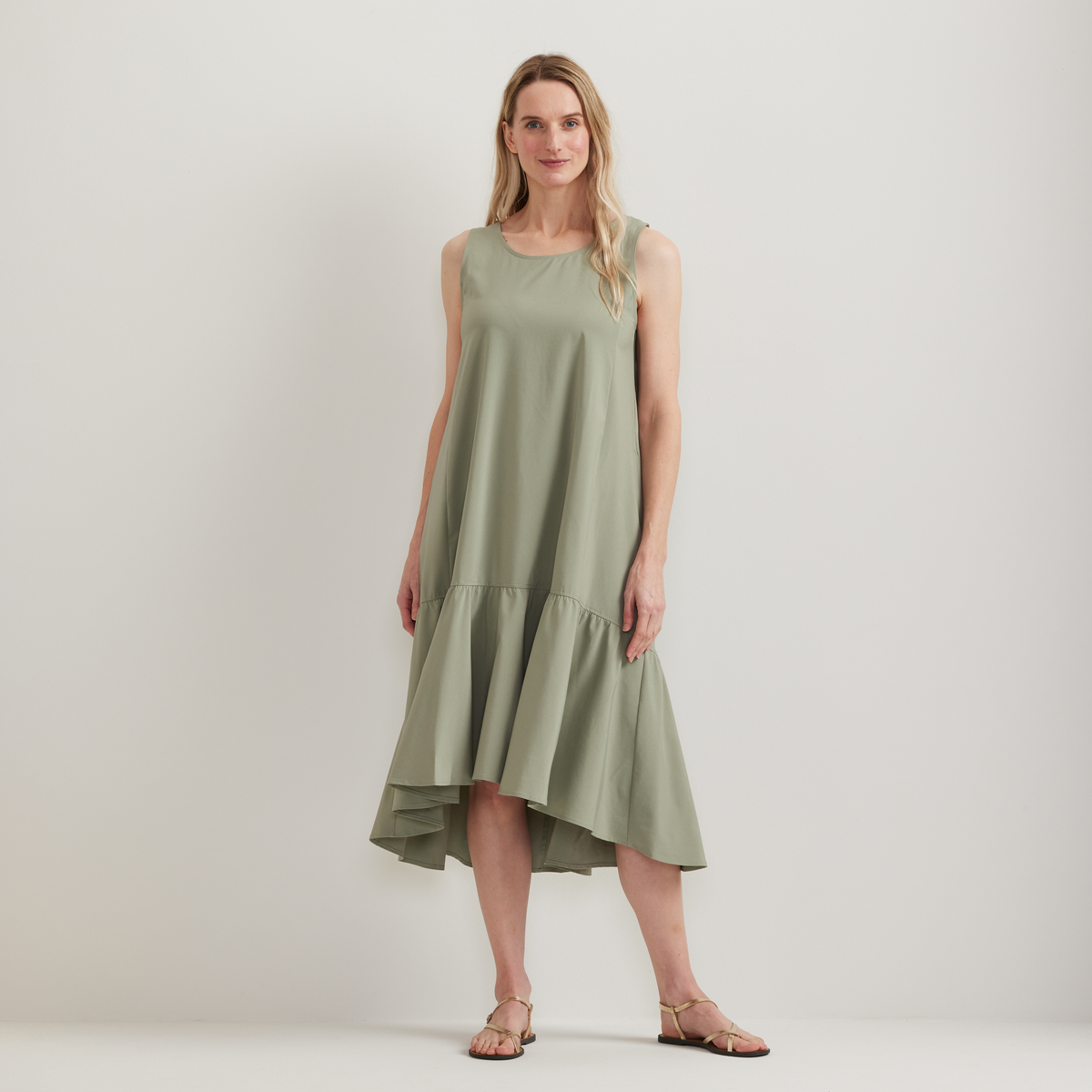 Sage green sleeveless midi dress with tiered skirt and asymmetrical hemline on a model.