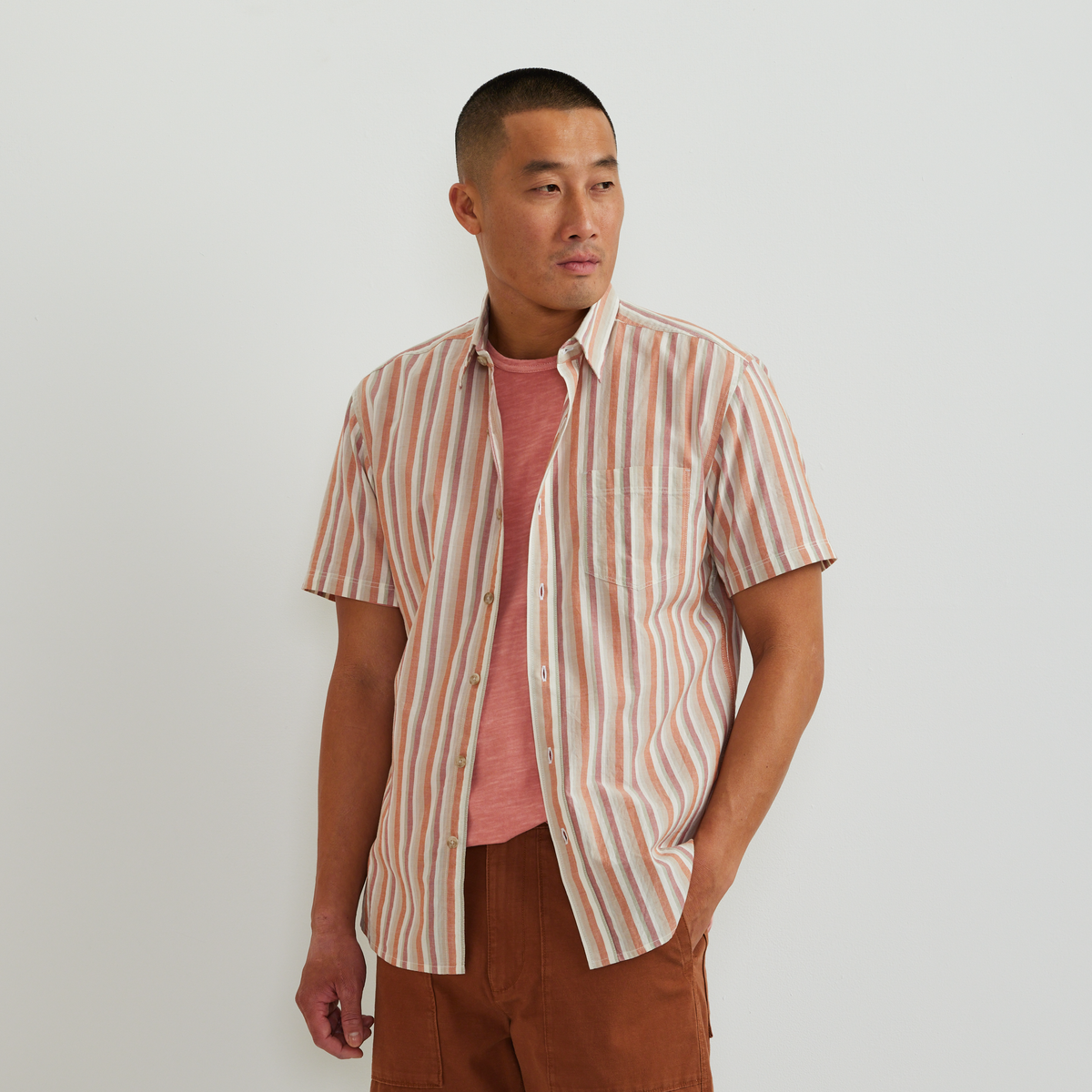 Men's short-sleeve button-up shirt with vertical coral and white stripe pattern, worn over a pink t-shirt.