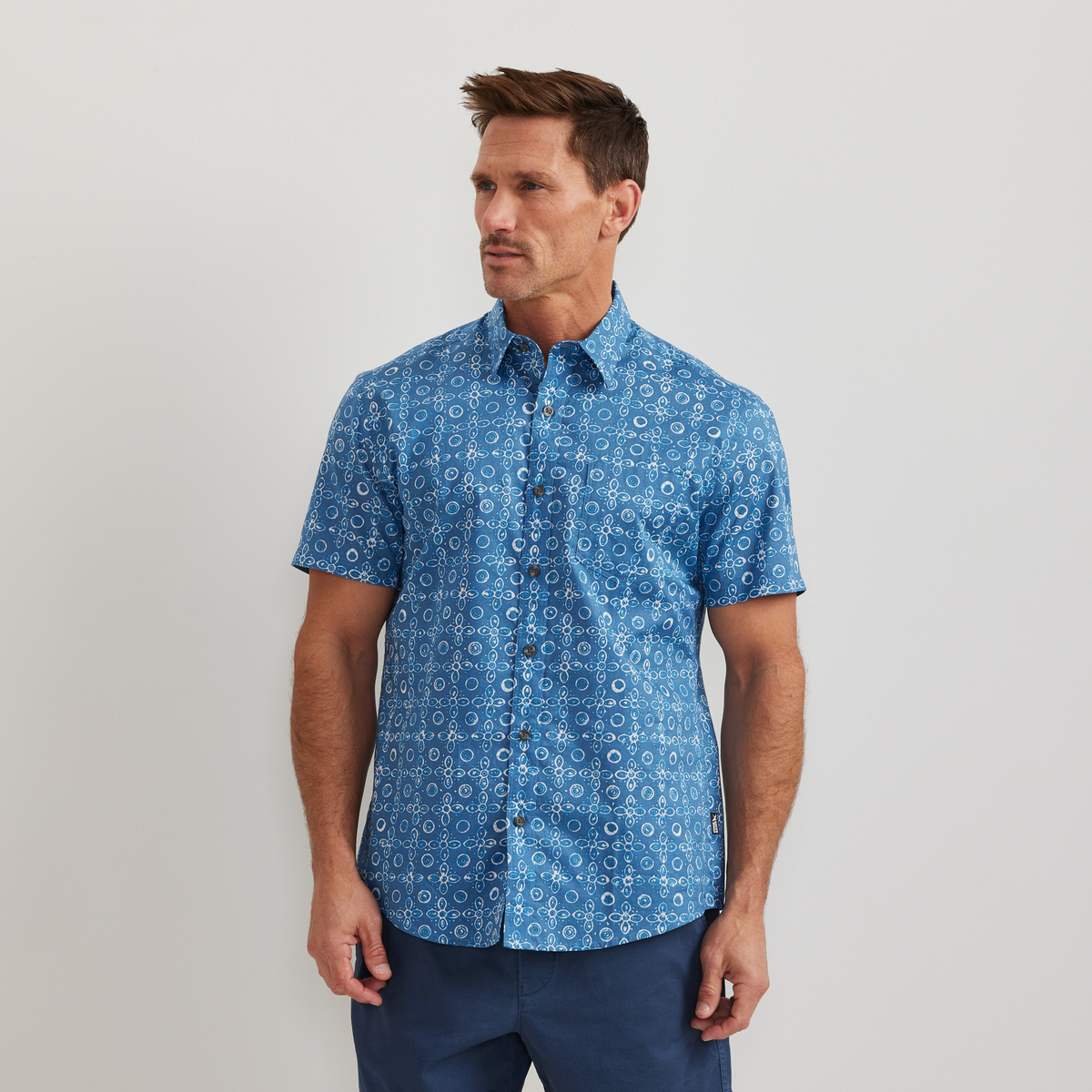 Men's blue short-sleeve shirt with small circular and geometric print pattern throughout.