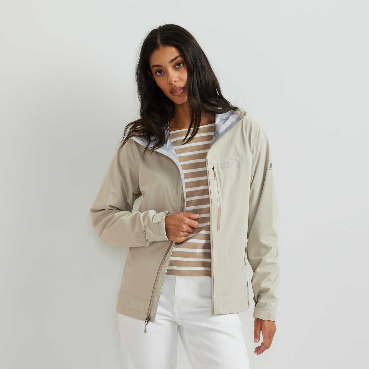 Beige hooded rain jacket with white striped shirt underneath and white pants.