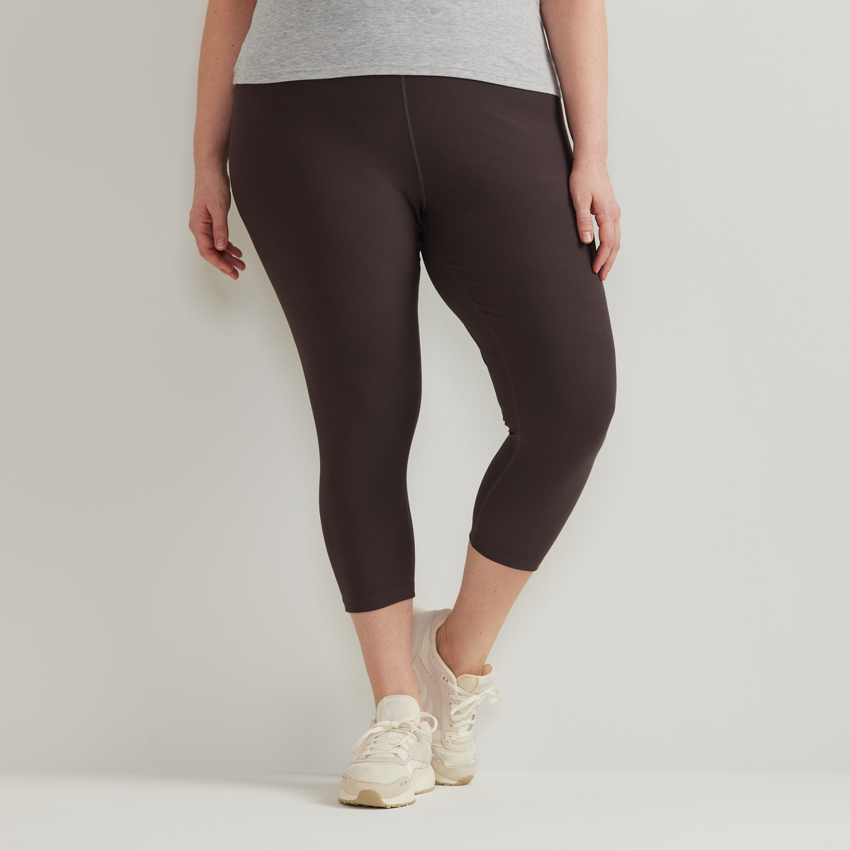 Woman wearing black high-rise capri leggings with gray tank top and cream sneakers.