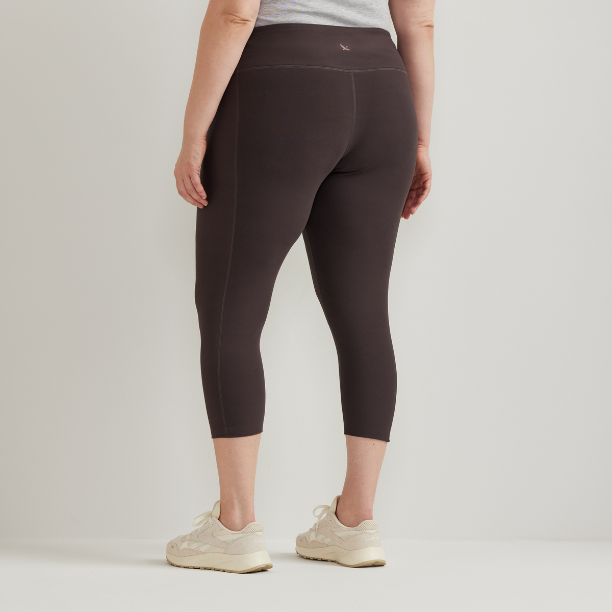 Black high-rise capri leggings with side seam detail, shown from back view on model wearing gray shirt and cream sneakers.